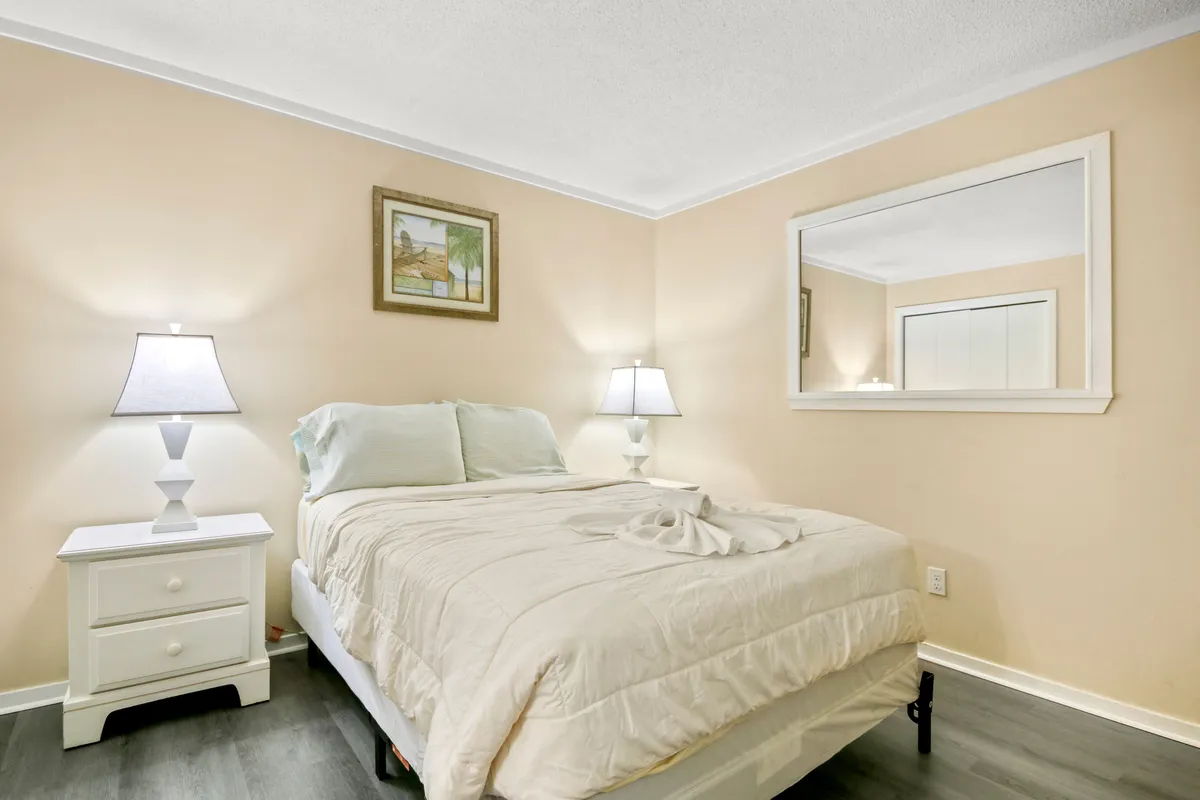 A tranquil primary bedroom with a neatly made bed, soft lighting from bedside lamps, a mirror, and a tasteful painting on the wall. The calming décor and plush bedding create a serene atmosphere, ideal for rest and relaxation.