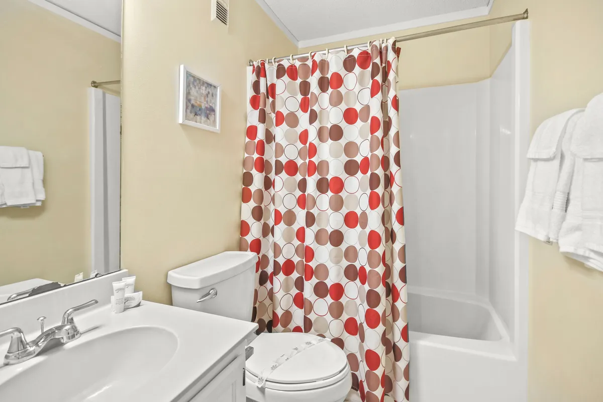 A cheerful bathroom featuring a colorful shower curtain, a clean sink and faucet, and a toilet. The space feels fresh, welcoming, and practical for daily routines.