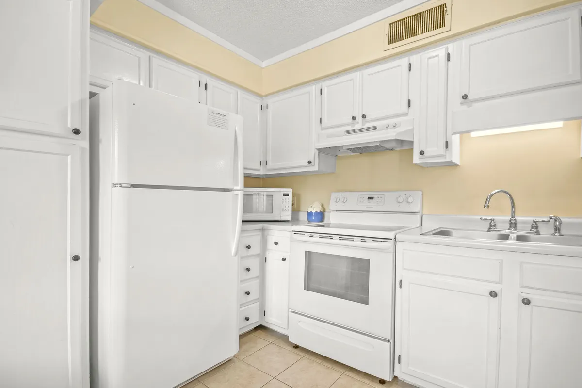 A bright, inviting kitchen with white appliances, light yellow walls, and clean countertops. The space is tidy and well-lit, suggesting a practical layout perfect for meal prep and family gatherings.