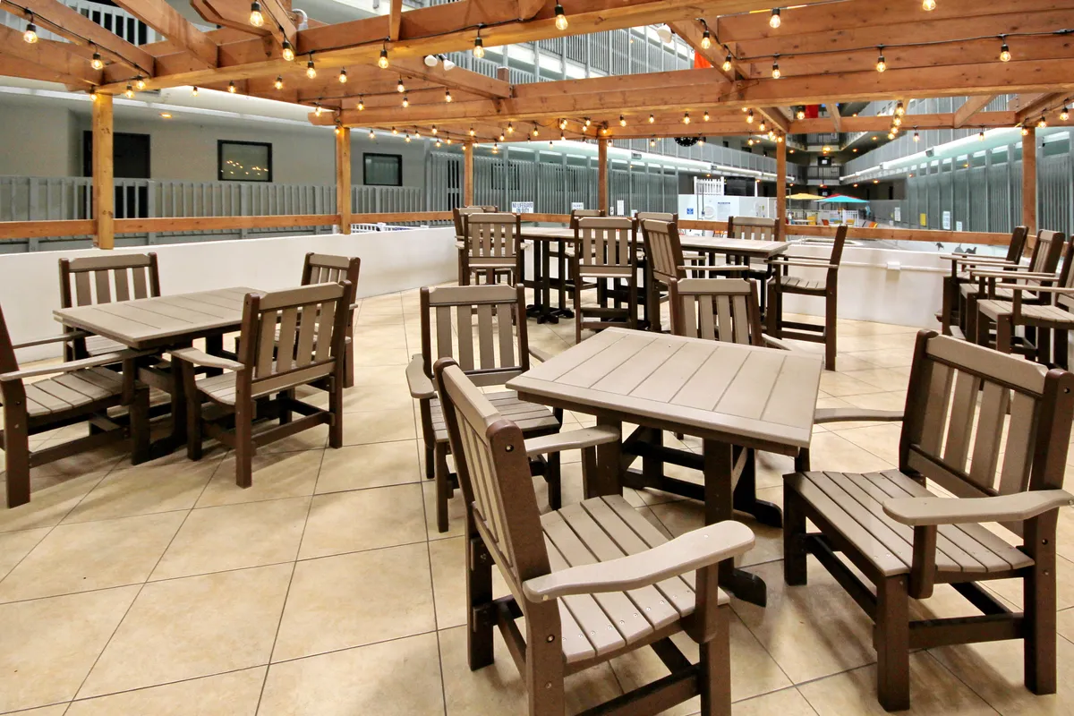 A spacious, warmly lit dining area with wooden tables and chairs arranged under string lights. The open layout invites large groups to gather for meals, celebrations, or casual conversation, suggesting flexibility for different types of group activities.
