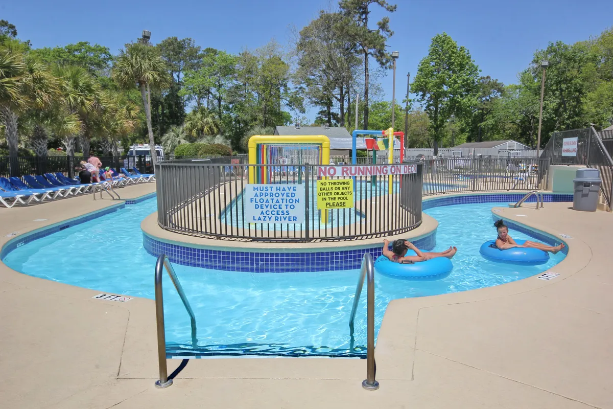 A lively scene at the expansive resort pool area, featuring a lazy river, children’s play zone, and plenty of poolside loungers. The energy is vibrant, with families and children enjoying water activities under the sun.
